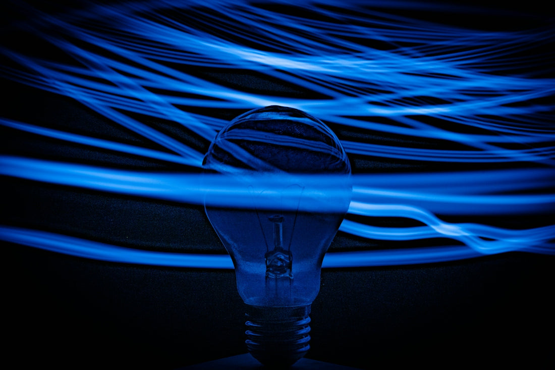 A light bulb surrounded by long exposure blue light trails against a dark background