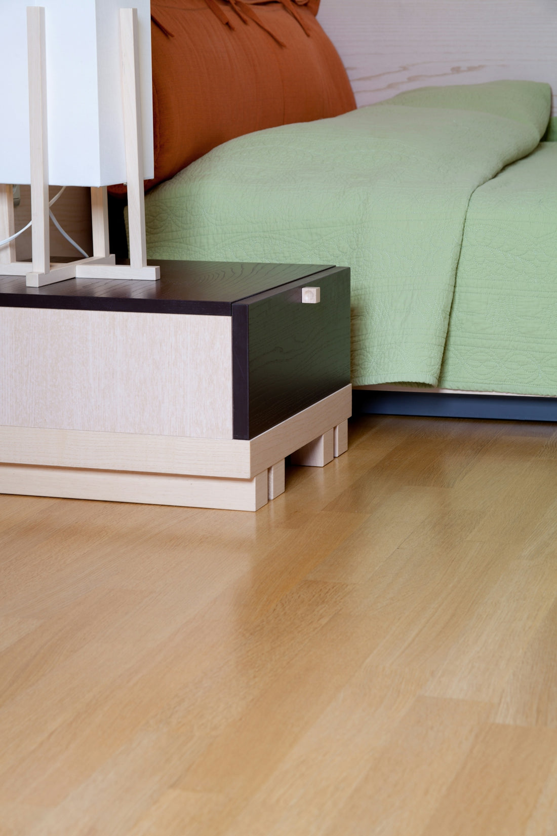 A bed sitting next to a night stand on a hard wood floor