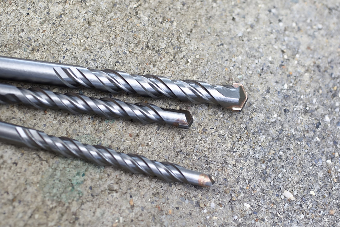 Three metal drill bits on a concrete surface
