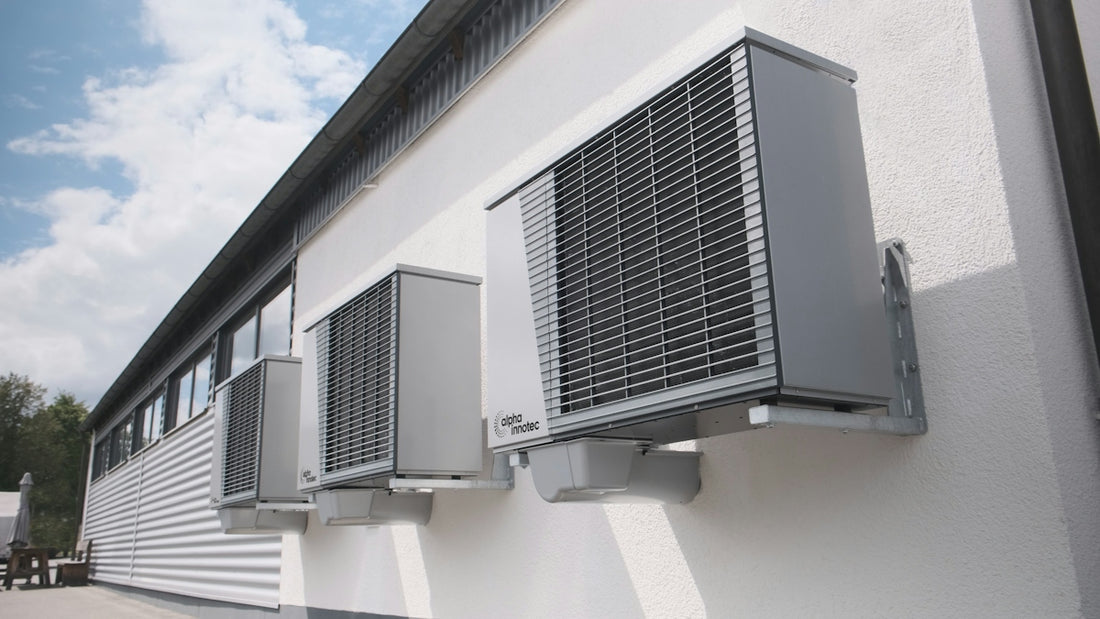Three gray air conditioning units mounted on a white wall