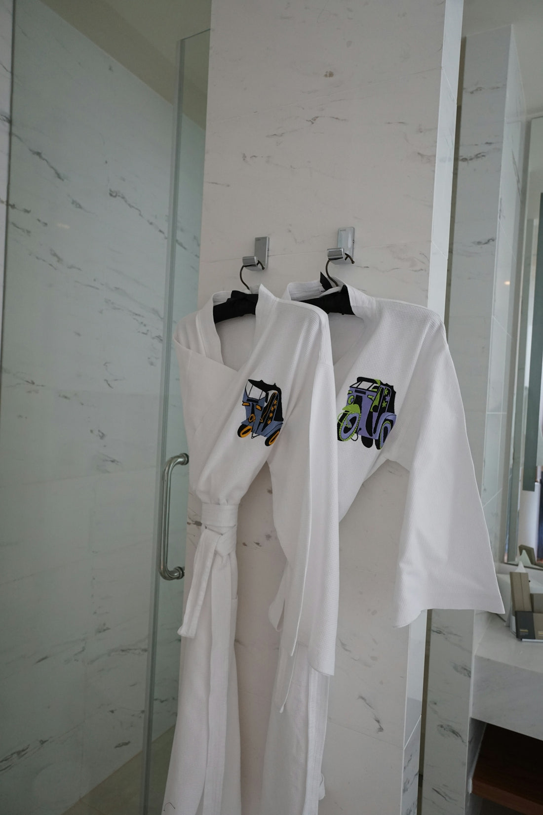 Two white robes hanging on hooks in a bathroom.