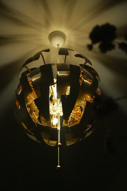 A spherical pendant light with gold interior panels casting shadows on the ceiling.