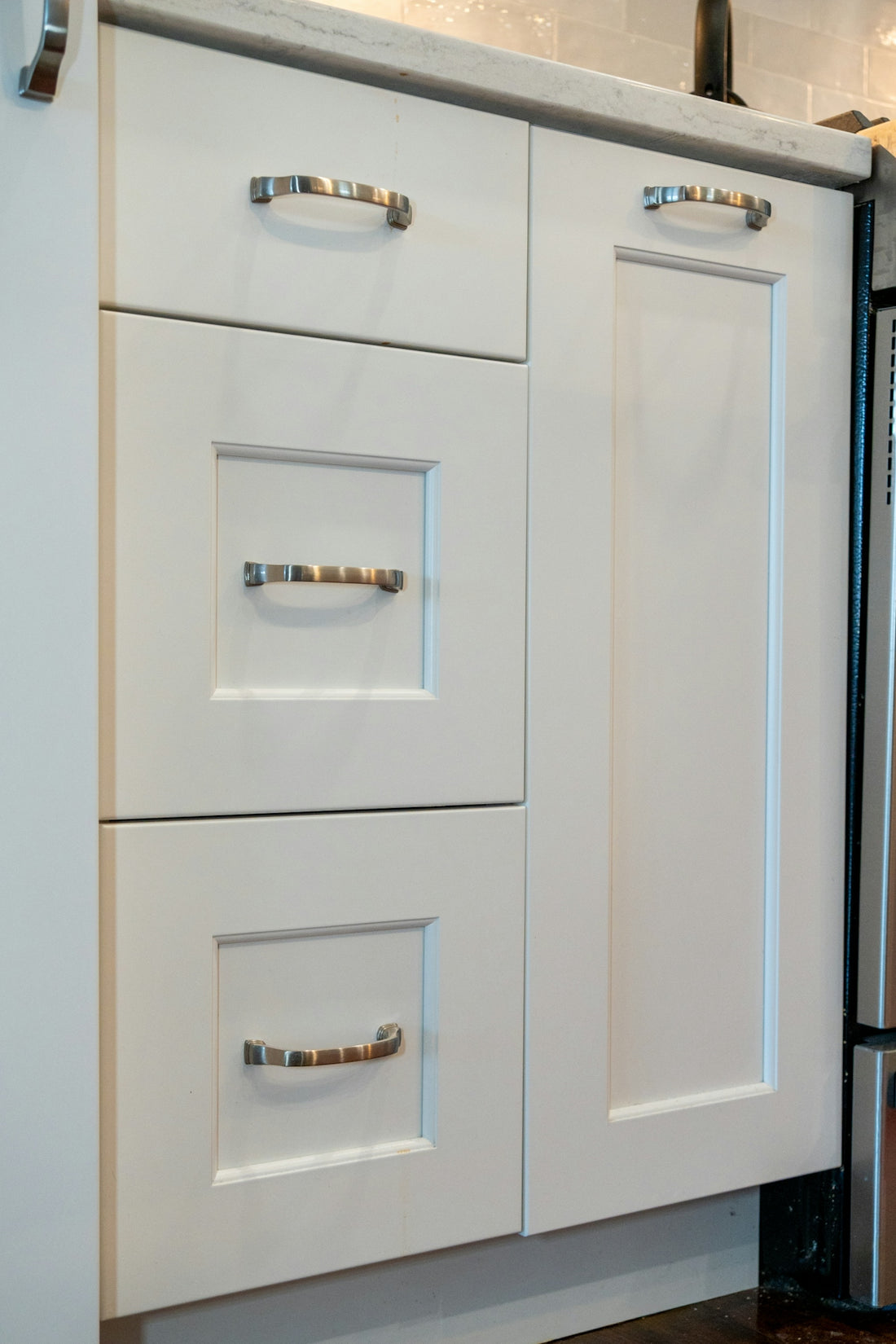 White kitchen cabinets with silver metal handles and a marble countertop