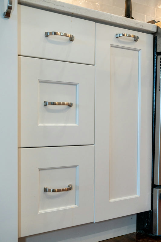 White kitchen cabinets with silver metal handles and a marble countertop