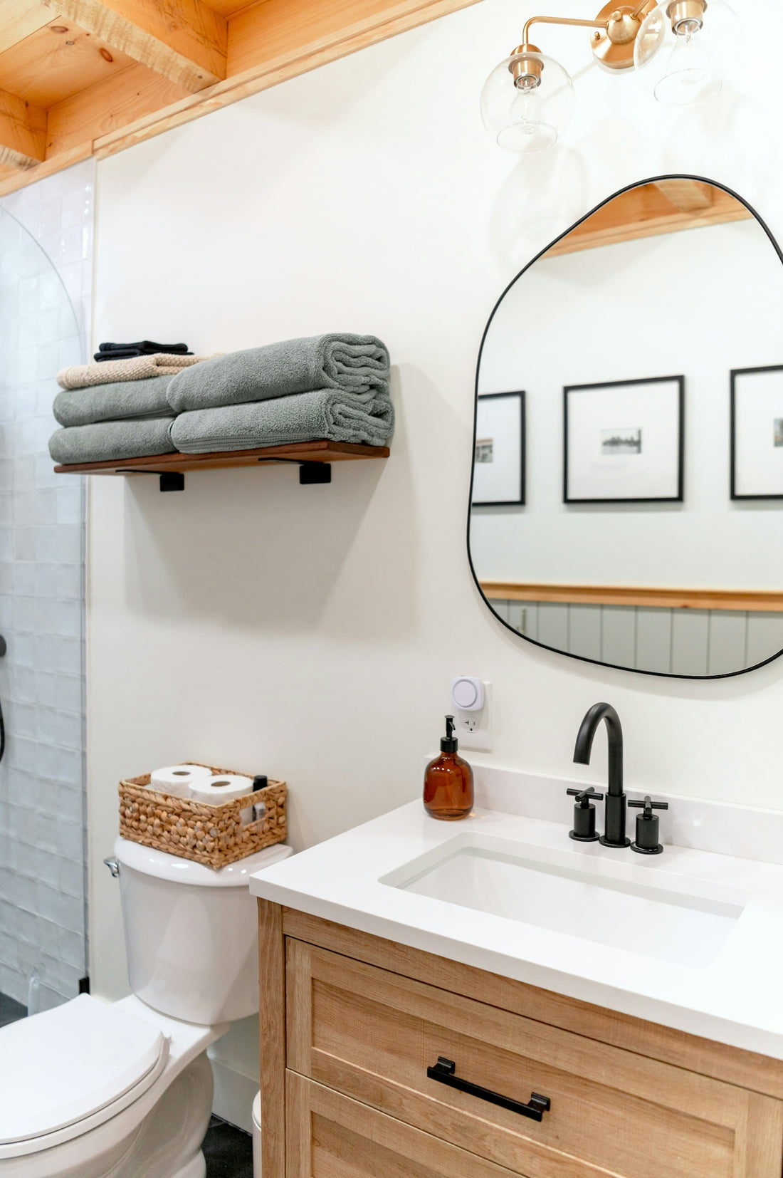 A bathroom with a wooden vanity, white sink, and an irregular mirror on a wall